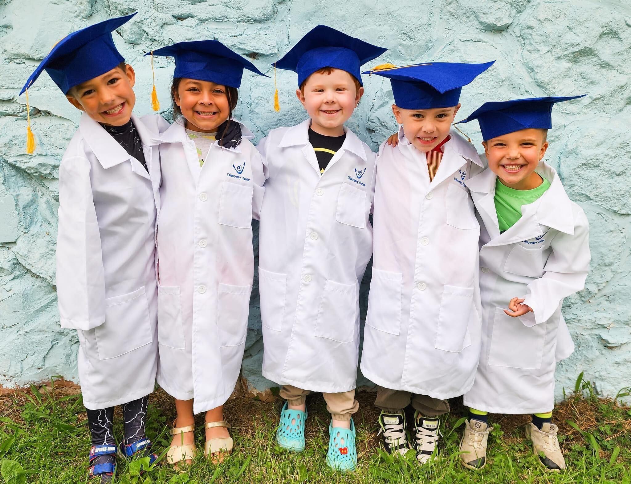 Children in graduation caps and lab coats celebrating their educational achievements